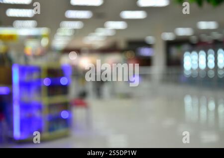 Immagine sfocata di un centro commerciale interno o di un supermercato con effetto bokeh nelle aree luminose del soffitto e degli stand commerciali. Immagine sfocata di Foto Stock
