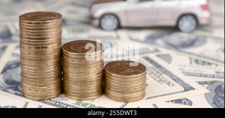 Un modello di auto giocattolo in pile di monete d'oro si trova su molte banconote da un dollaro, un tasso fisso per il prestito di un'auto o un risparmio di denaro per comprare un'auto, commerciare con denaro contante, finanziare Foto Stock