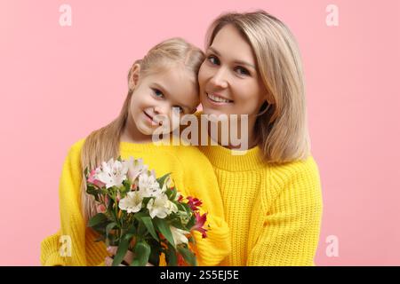 Donna felice con sua figlia e bouquet di fiori di alstroemeria su sfondo rosa. Festa della mamma Foto Stock