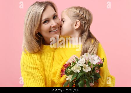 Donna felice con sua figlia e bouquet di fiori di alstroemeria su sfondo rosa. Festa della mamma Foto Stock