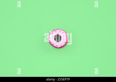 Una piccola ciambella di plastica giace su uno sfondo color pastello. Composizione minima per la posa piatta. Vista dall'alto. Una piccola ciambella di plastica giace su un pastello Foto Stock