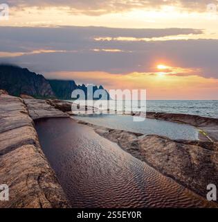 La spiaggia sassosa con bagni di marea a Ersfjord, Senja, Norvegia. Estate giorno polare notte costa. I denti di drago di roccia nel lontano. Foto Stock