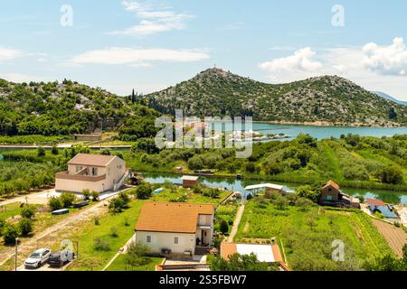 Una vista panoramica di un villaggio costiero con case circondate dal verde e una montagna sullo sfondo sotto un cielo azzurro cristallino, Rogotin, Croazia Foto Stock