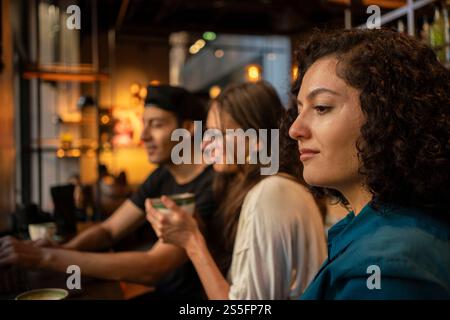 Tre amici o colleghi che condividono un momento in un accogliente bar, con un uomo che digita su un laptop e un'altra donna che si occupa di conversazione, Berlino, Germania Foto Stock