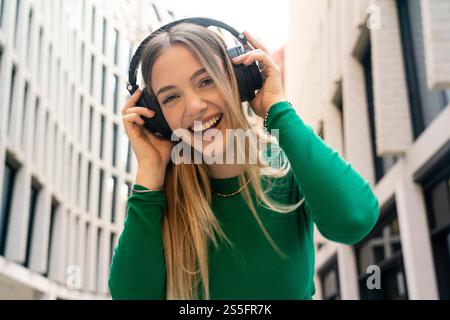 Una donna sorridente con un top verde ama la musica con le sue cuffie in un ambiente urbano, Berlino, Germania Foto Stock