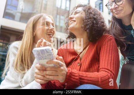 Tre donne condividono un momento di gioia insieme mentre guardano uno smartphone, Berlino, Germania Foto Stock