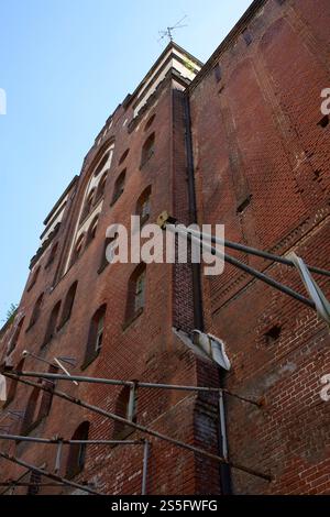 Vista verso l'alto di un alto edificio abbandonato in mattoni con finestre multiple e tubazioni esterne che si affacciano su un cielo limpido, Berlino, Germania Foto Stock