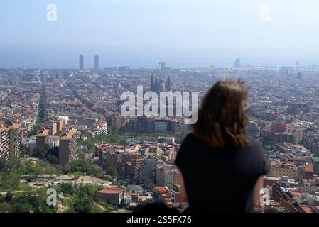 Una donna guarda su un vasto paesaggio urbano con edifici prominenti e una costa in lontananza, Barcellona, Spagna Foto Stock