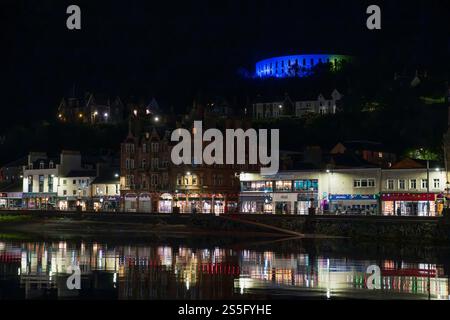 Oban, Argyll & Bute, porto e terminal dei traghetti per le isole sulla costa occidentale scozzese. Il lungomare di notte con la Torre McCaig illuminata di blu. Foto Stock