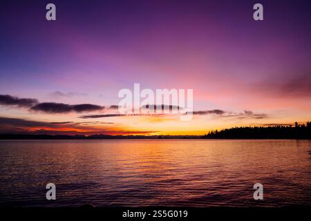 Un tramonto mozzafiato su un lago calmo con la silhouette di una riva alberata. Il cielo vibrante passa dal viola intenso alle tenui tonalità arancio e rosa, Norwegian Point, WA, USA Foto Stock