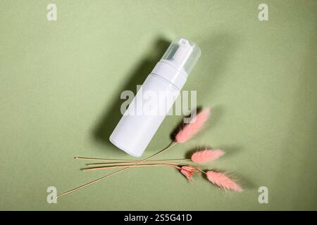 vista dall'alto di una bottiglia di plastica bianca chiusa con pompa vuota e di spikelets rosa essiccati naturali su fondo di carta cachi Foto Stock