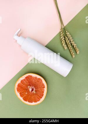 vista dall'alto di una bottiglia di plastica bianca a pompa vuota, metà di pompelmo fresco e orecchie essiccate naturali su sfondo di carta a colori Foto Stock
