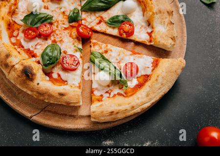 Pizza Margherita appena tagliata con basilico, mozzarella e pomodori ciliegini su un piatto rustico Foto Stock