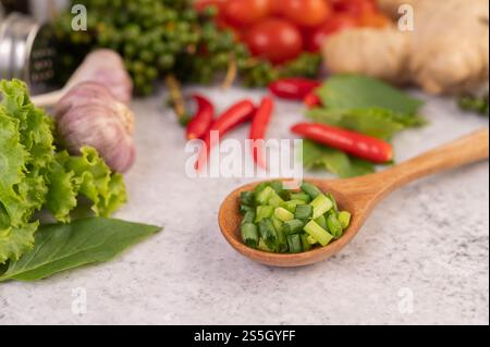 Cipolla primaverile tritata su un cucchiaio di legno con peperoni e pomodori su un pavimento di cemento bianco. Foto Stock