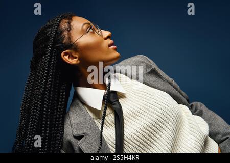 Una bella giovane donna sfoggia i suoi capelli intrecciati e il suo outfit elegante mentre guarda con attenzione. Foto Stock