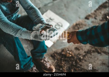 Mendicante seduto sotto il cavalcavia con una macchina per carte di credito e carte di credito. Foto Stock