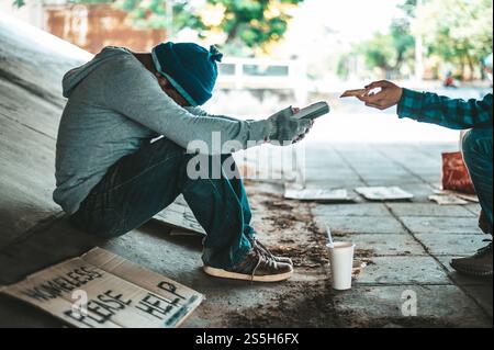 Mendicante seduto sotto il cavalcavia con una macchina per carte di credito e carte di credito. Foto Stock