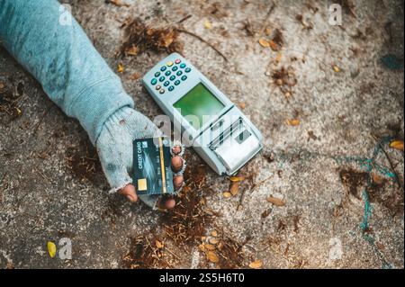Mendicante seduto sotto il cavalcavia con una macchina per carte di credito e carte di credito. Foto Stock