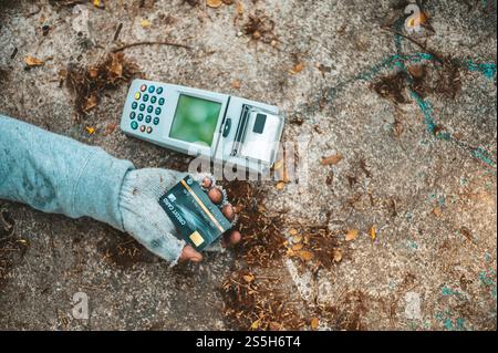 Mendicante seduto sotto il cavalcavia con una macchina per carte di credito e carte di credito. Foto Stock