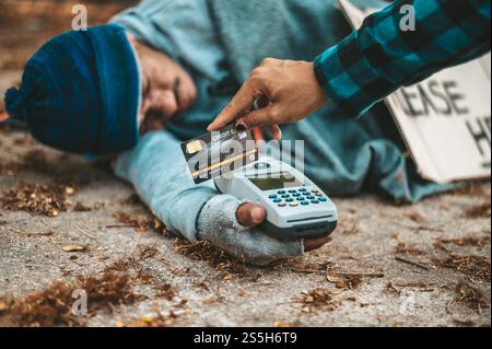 Mendicante seduto sotto il cavalcavia con una macchina per carte di credito e carte di credito. Foto Stock