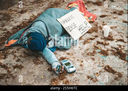 Mendicante seduto sotto il cavalcavia con una macchina per carte di credito e carte di credito. Foto Stock