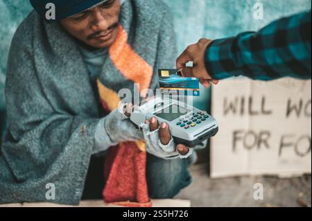Mendicante seduto sotto il cavalcavia con una macchina per carte di credito e carte di credito. Foto Stock