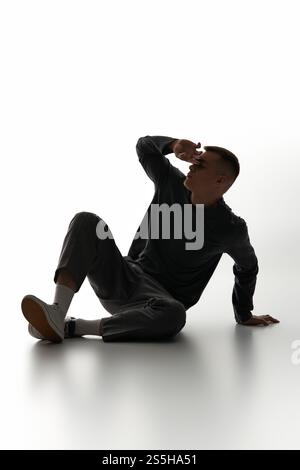 Un giovane uomo mette in posa il pavimento con cura, mettendo in risalto il suo stile su uno sfondo chiaro. Foto Stock