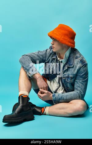 Un bel giovane uomo siede comodamente sul pavimento, mostrando il suo vestito elegante e il suo cappello vivace. Foto Stock