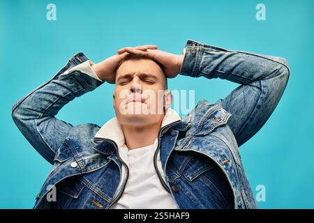 Il giovane uomo con una giacca in denim alla moda si rilassa su uno sfondo luminoso, esprimendo gioia. Foto Stock