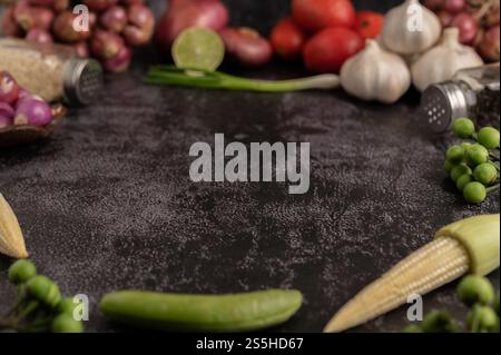 Baby corn, piselli verdi, melanzane, aglio, pomodoro, calce, scallio e cipolla rossa poste su un pavimento di cemento nero Foto Stock
