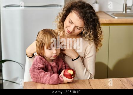 Madre e figlia ricci condividono un momento tenero mentre si godono una mela a casa. Foto Stock