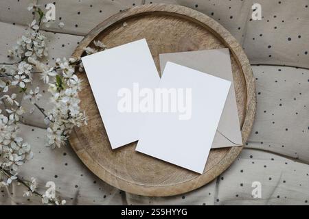 Cartoleria primaverile ancora vita. Due biglietti d'auguri vuoti, mockup di inviti su vassoio di legno Involucro di creazione. Prugna ciliegina sfocata in fiore Foto Stock