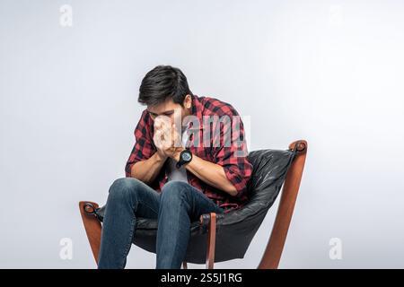 L'uomo con una camicia a righe si siede malato e si siede su una sedia e si incrocia le braccia. Foto Stock