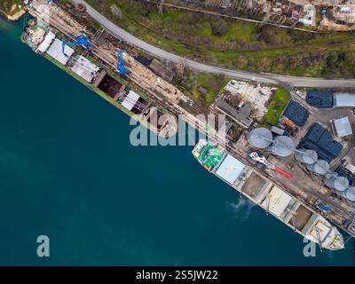 Ampia vista aerea di due navi da carico attraccate fianco a fianco in un vivace porto industriale, che mette in evidenza le infrastrutture e i dintorni. Foto Stock