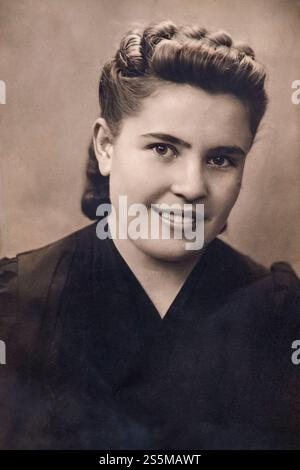 Ritratto vintage di una donna sorridente con i capelli intrecciati e una camicetta scura, che mostra la moda e l'acconciatura europea degli anni '1940 del XX secolo Foto Stock