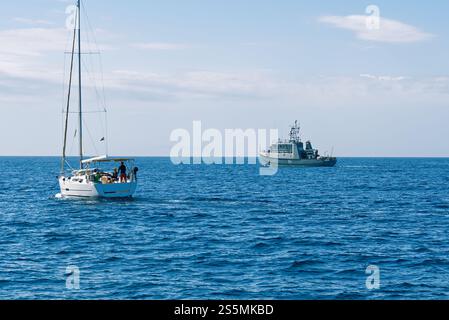 Ispezione di una piccola barca a vela con tre persone a bordo di una nave delle forze armate in mare aperto oggi Foto Stock