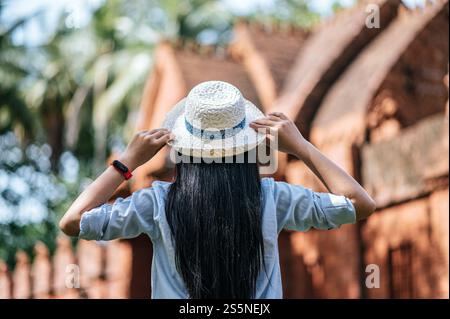 Vista posteriore, giovane donna con lunghi capelli neri che indossa un cappello, sfondo sfocato con sito antico, spazio per copiare Foto Stock