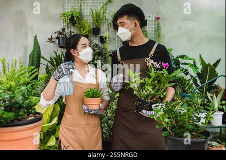 Ritratto giovane coppia asiatica di giardinieri che indossa il grembiule usano le attrezzature da giardino e aiutano a prendersi cura della pianta domestica in negozio insieme, piccola impresa con Foto Stock