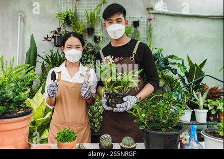 Ritratto giovane coppia asiatica di giardinieri che indossa il grembiule usano le attrezzature da giardino e aiutano a prendersi cura della pianta domestica in negozio insieme, piccola impresa con Foto Stock