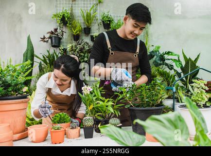 Ritratto giovane coppia asiatica di giardinieri che indossa il grembiule usano le attrezzature da giardino e aiutano a prendersi cura della pianta domestica in negozio insieme, piccola impresa con Foto Stock