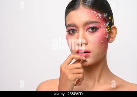 Donna che indossa trucco e decorazioni rosa sul viso. Isolato su sfondo bianco Foto Stock