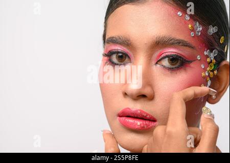 Donna che indossa trucco e decorazioni rosa sul viso. Isolato su sfondo bianco Foto Stock