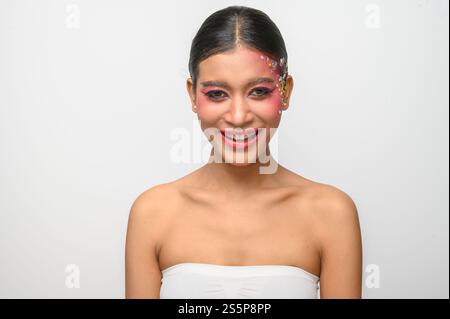 Donna che indossa trucco e decorazioni rosa sul viso. Isolato su sfondo bianco Foto Stock
