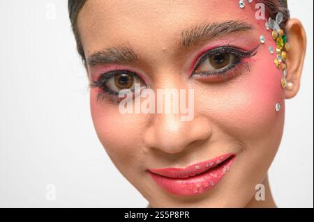 Donna che indossa trucco e decorazioni rosa sul viso. Isolato su sfondo bianco Foto Stock