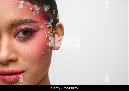 Donna che indossa trucco e decorazioni rosa sul viso. Isolato su sfondo bianco Foto Stock