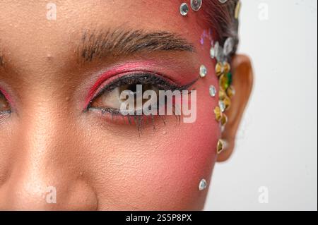 Donna che indossa trucco e decorazioni rosa sul viso. Isolato su sfondo bianco Foto Stock