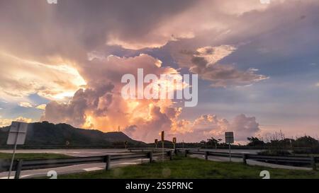 Una splendida vista delle nuvole dorate del tramonto che illuminano il cielo, proiettando un caldo bagliore su una tranquilla autostrada circondata da verdi colline. Foto Stock