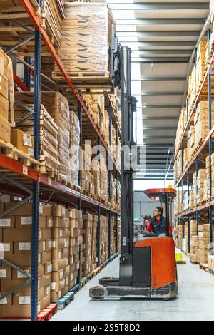 Foto verticale a tutta lunghezza di un lavoratore latino che guida un carrello elevatore in un magazzino Foto Stock