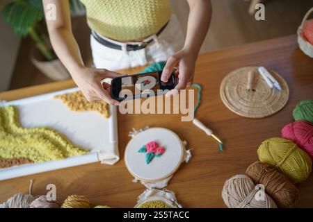 Donna asiatica che scatta foto smartphone Punch Needle. postazioni telefoniche sui social network in officina. Ambiente di lavoro di design progetto artigianale fai da te Foto Stock
