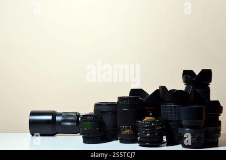 Molti obiettivi diversi per fotocamere reflex si trovano su una scrivania incolore. Immagine di sfondo per un biglietto da visita di un fotografo o di un fornitore di attrezzature fotografiche. Foto Stock